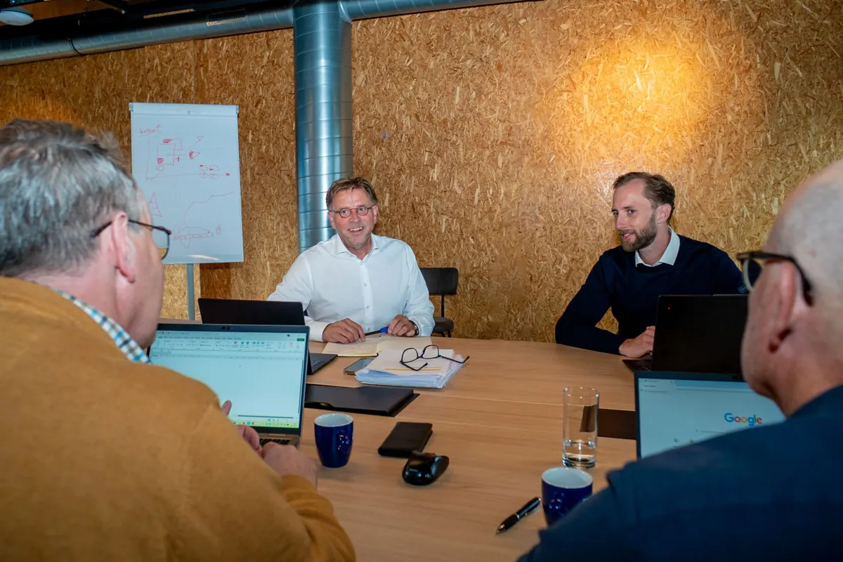 Working session at a table with laptops and a flip chart, Paul Hoffman in conversation with three participants