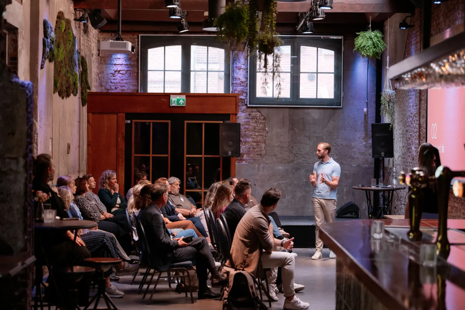 Paul Hoffman spreekt voor een zaal met toehoorders in een oud pand met bakstenen muren